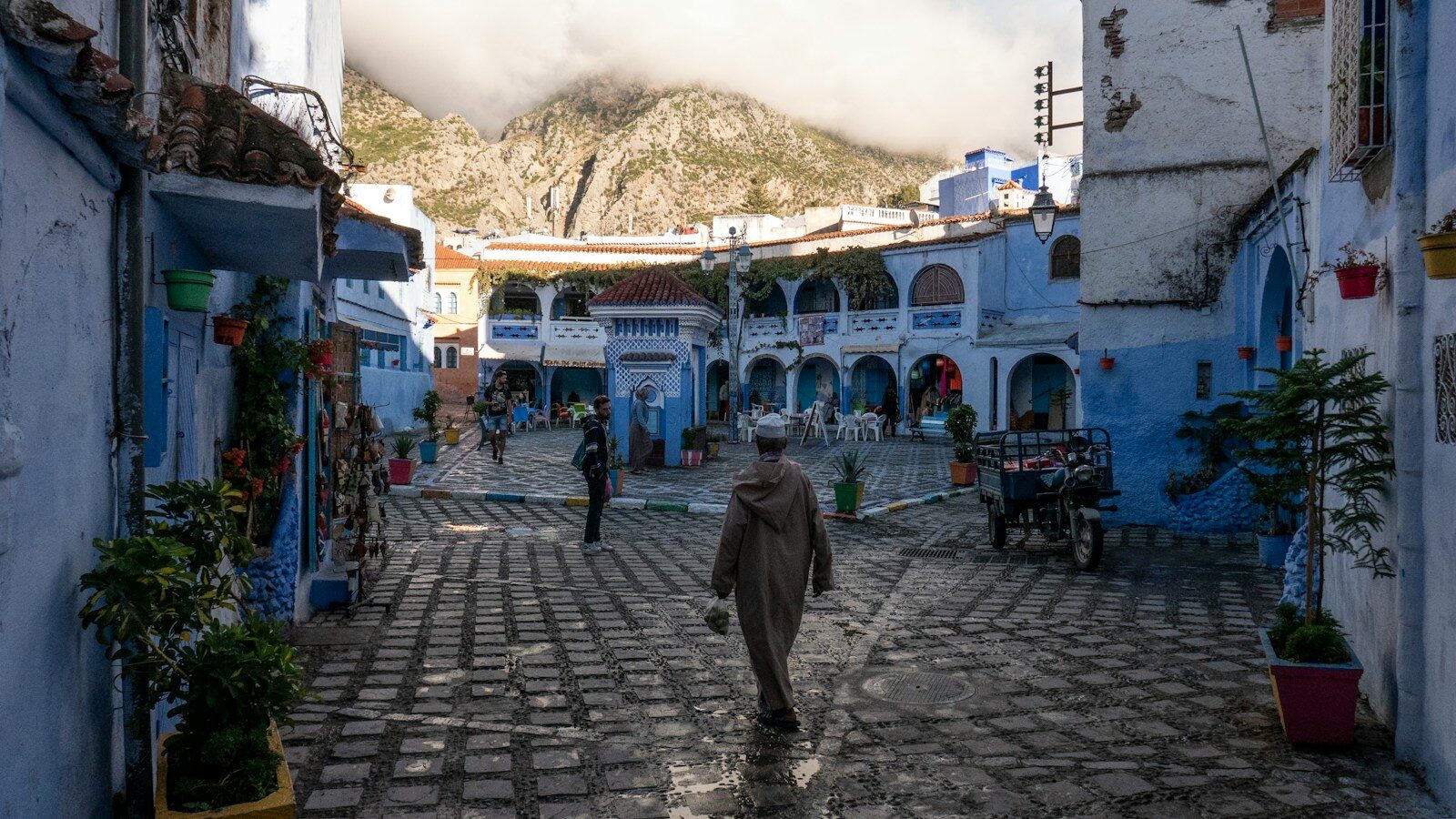 Visitors walking a blue medina street in Chaouen, Morocco, between the old gates