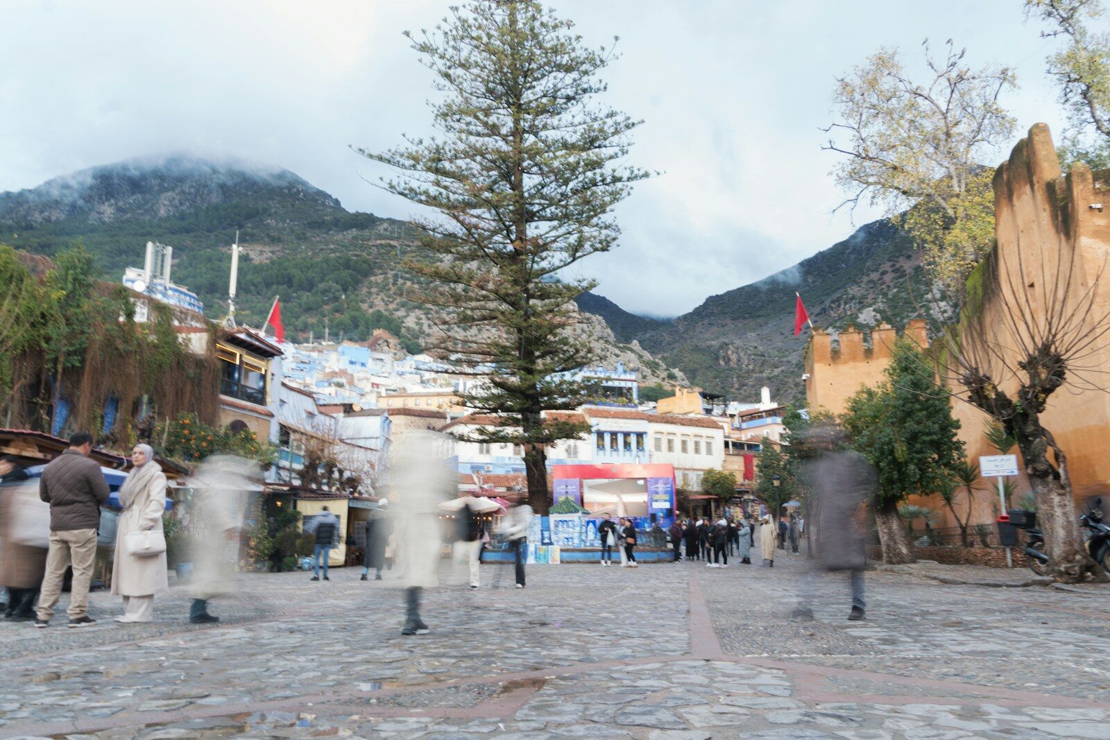 People walking in Outa el Hammam square near the Chefchaouen kasbah with mountains behind