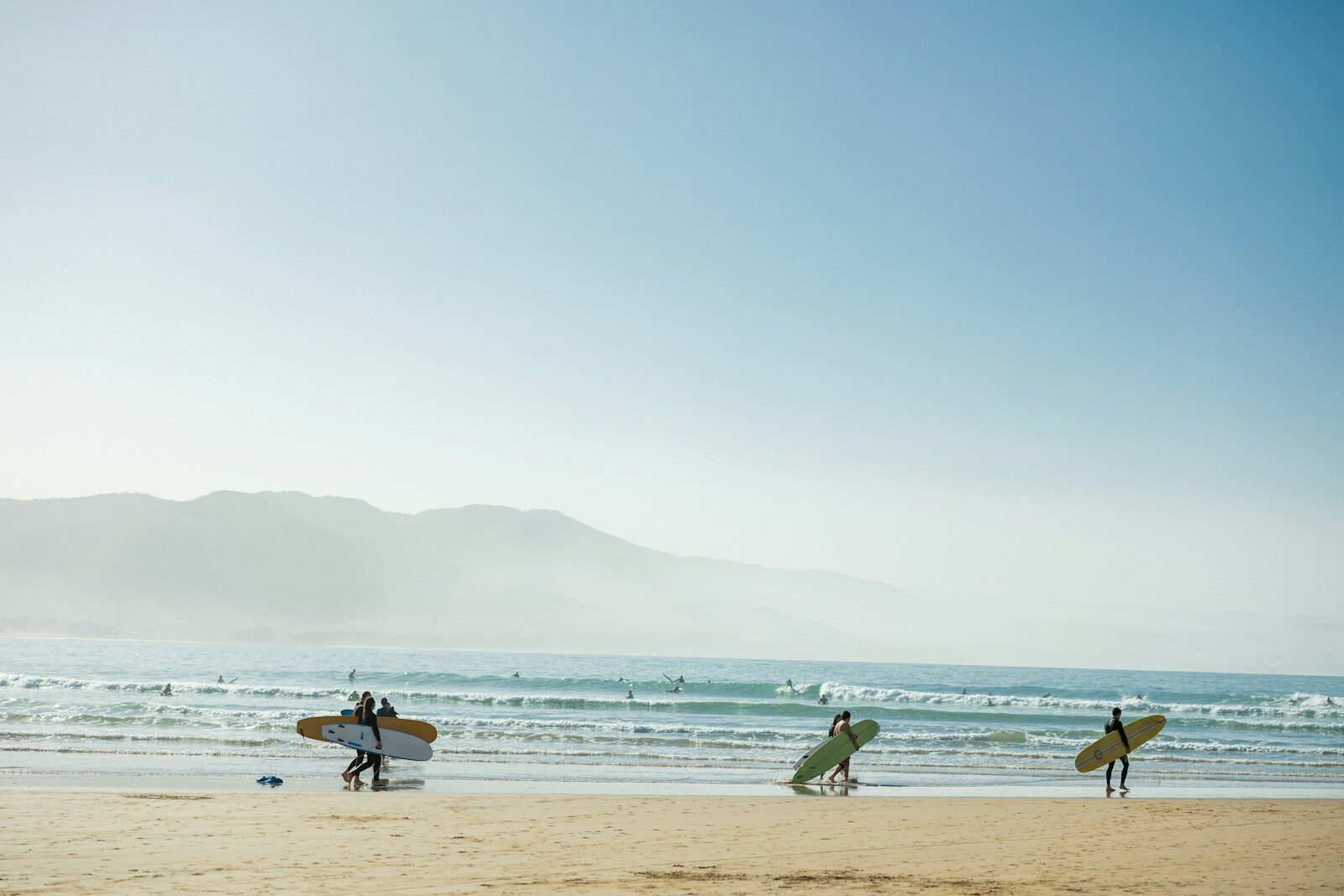 Surfers carrying boards across the sand on a Moroccan Atlantic beach, a common Essaouira surf scene