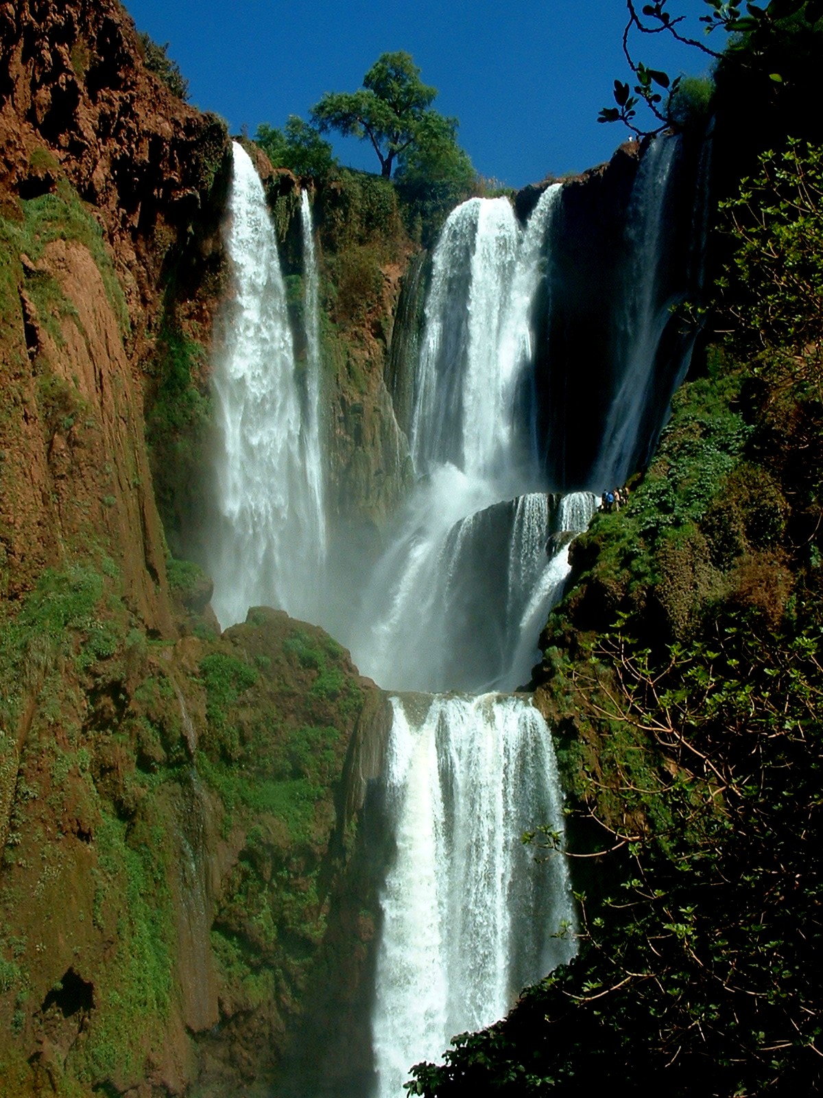 Ouzoud cascades tumbling over red tufa cliffs and green ledges in Morocco