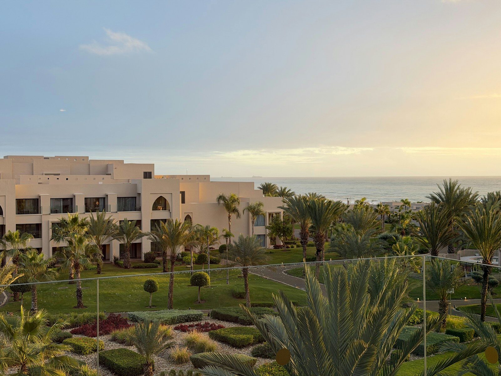 Taghazout Bay style resort buildings and palm trees by the ocean at sunset