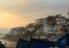 Taghazout Guide: Surf Camps, Beaches, Hotels and Where to Eat Taghazout village with white buildings and blue fishing boats at sunset