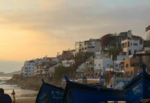 Taghazout Guide: Surf Camps, Beaches, Hotels and Where to Eat Taghazout village with white buildings and blue fishing boats at sunset